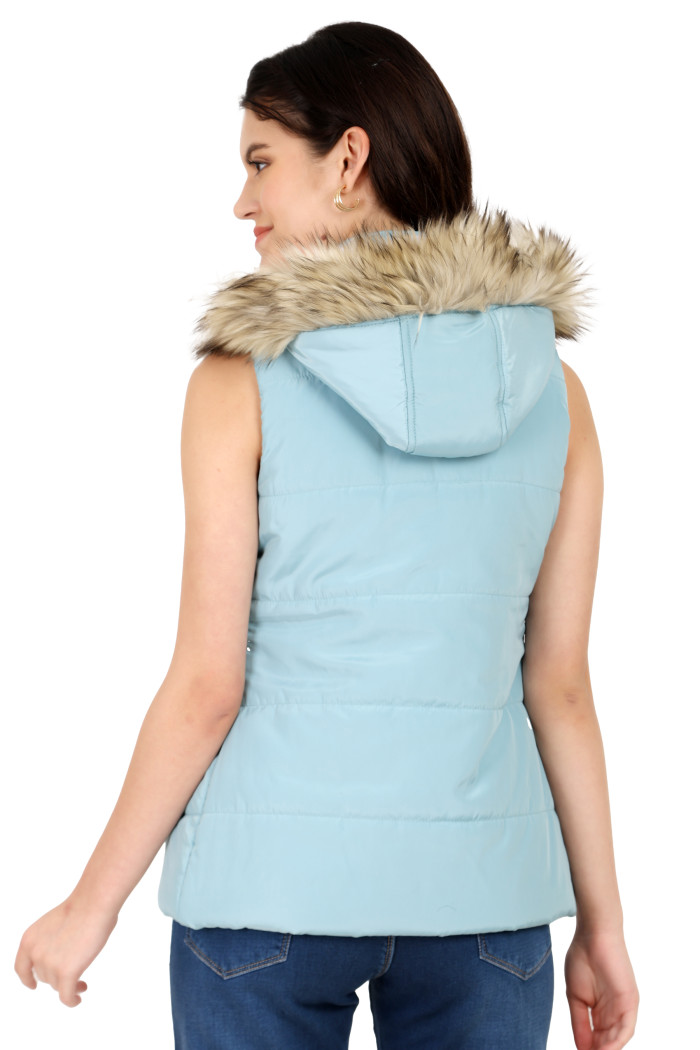 A back pose of a standing woman, wearing Trufit’s sea green half-sleeve quilted jacket with removable hood and blue jeans.